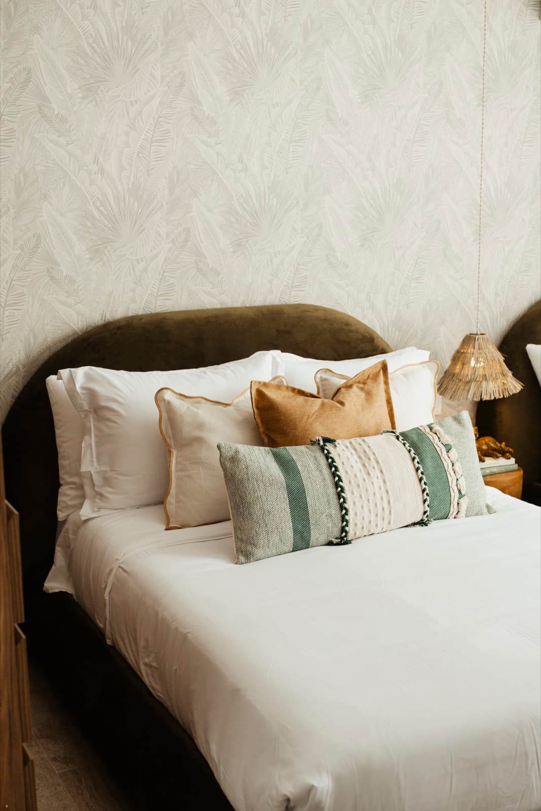 Turnkey Airbnb bedroom with an olive velvet headboard, layered cushions and a raffia sconce