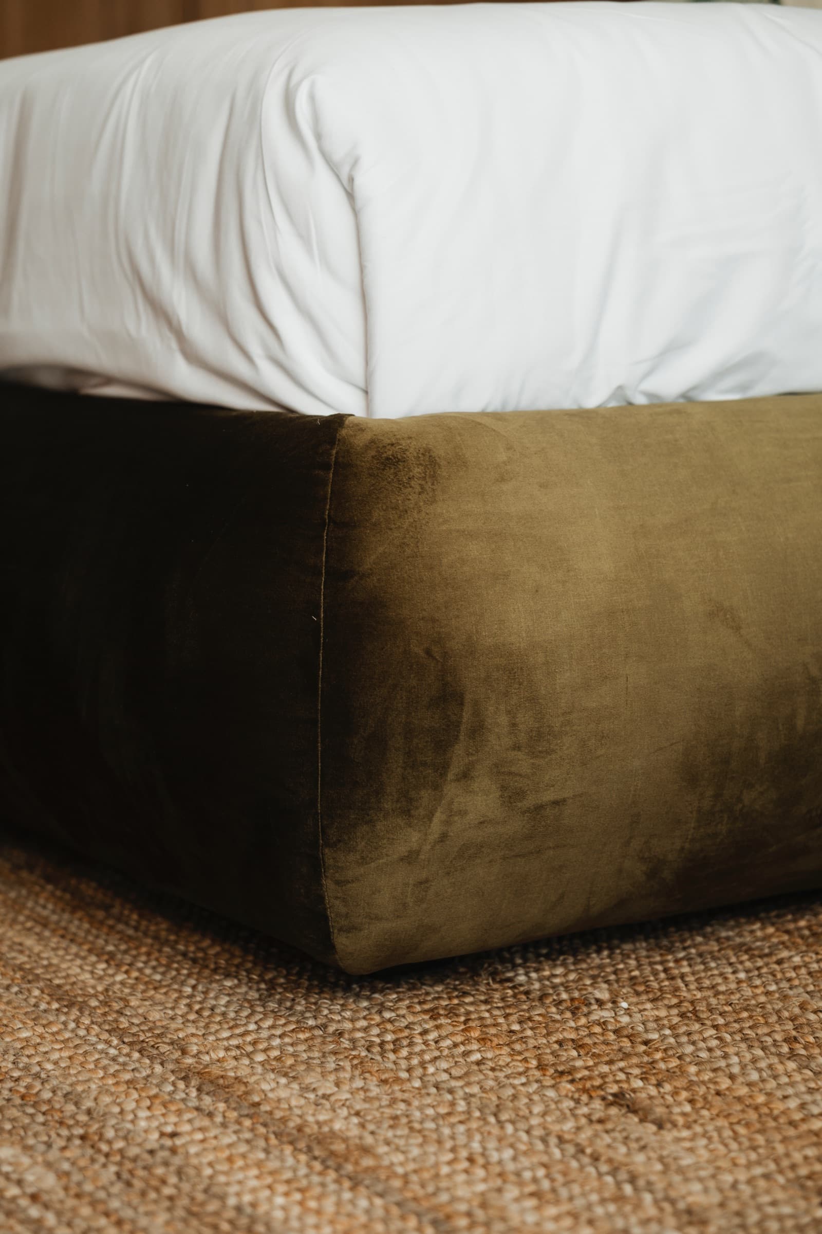 Bed with an olive velvet base and white linens on a jute rug